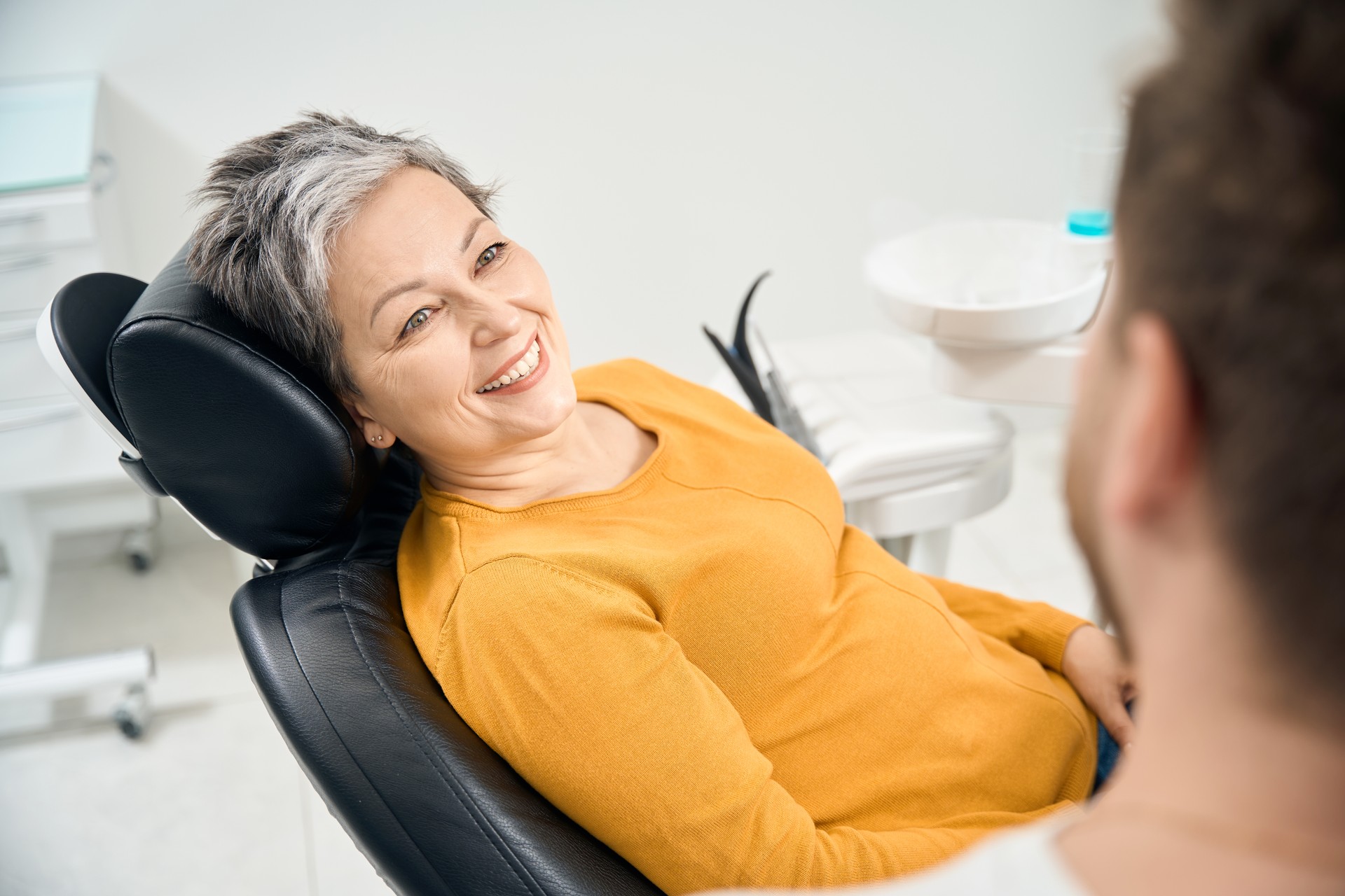 Woman client in her 50 looking at doctor stomatologist and smiling