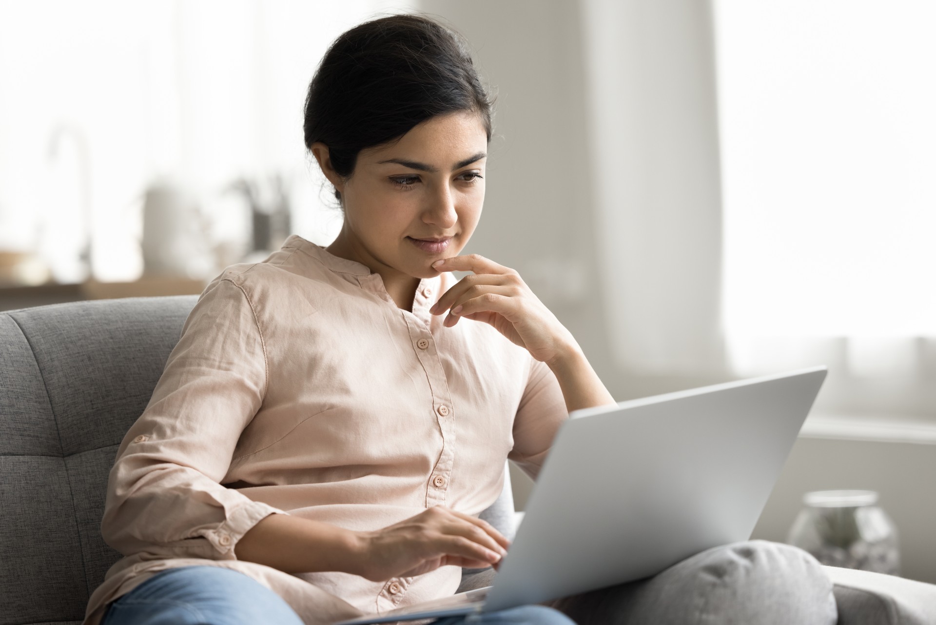 Pensive Indian woman learn program studying on-line seated on sofa